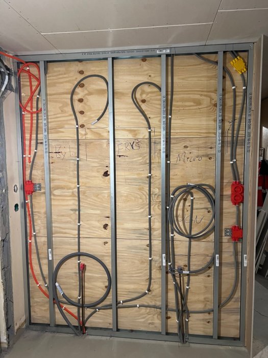 Elkabel installation för hemrenovering på en vägg med reglar och isolering, synliga markerade områden för framtida uttag.