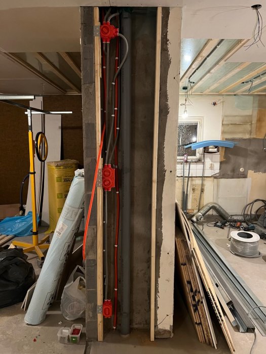 Renoveringsarbete visar elinstallation med röda kablar och eldosor i vägg, med isoleringsmaterial och träplankor intill.