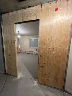 Plywood monterad i och runt en dörröppning i en byggnads korridor under renovering.