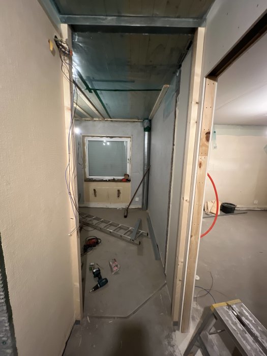 Pågående renovering visande oisolerade väggar och tak med synliga kablar samt byggverktyg på golvet.