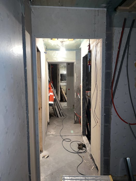 Renoveringsarbete med gipsskivor längs en korridor med synliga elektriska ledningar och byggmaterial på golvet.