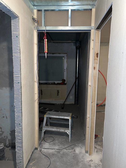 Renoveringsarbete i korridor med obehandlade väggar, isoleringsmaterial och en stege.