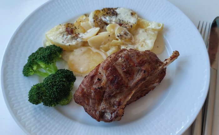 Grillat kött med ben, potatisgratäng och broccoli på en vit tallrik.