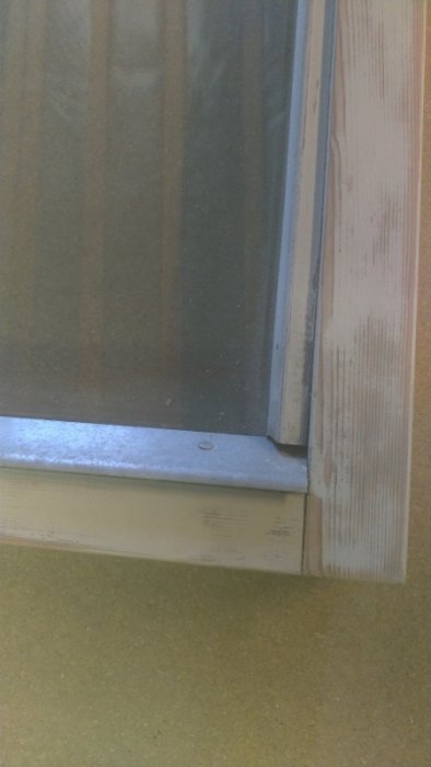 Del av ett äldre vridfönster med synliga slitage och i behov av målning, beläget vid en husvägg.