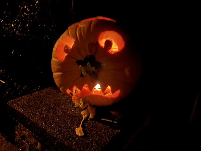 Utskuren pumpalykta med tända ljus inuti fotograferad i mörker.