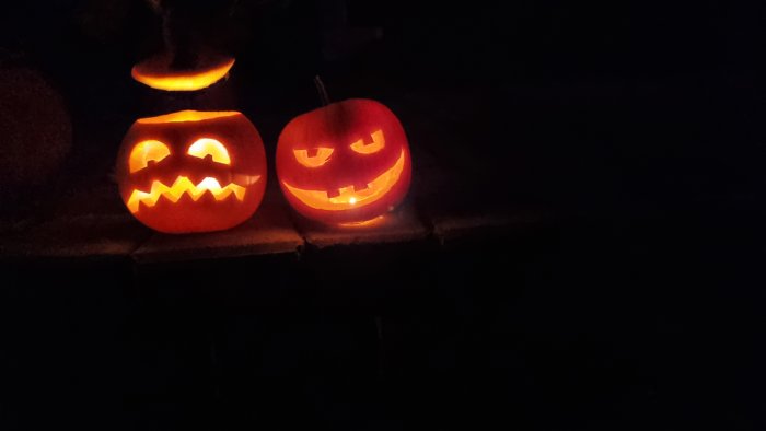 Två upplysta Jack-o'-lantern pumpor i mörkret.