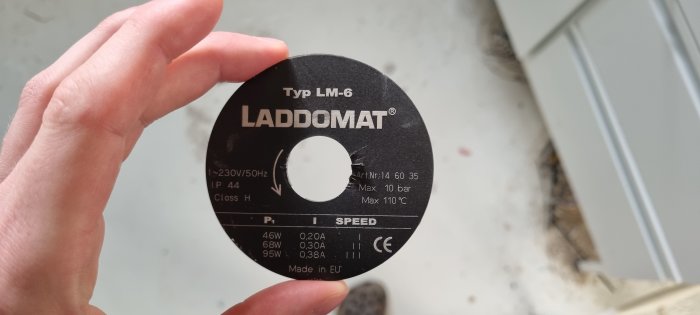 Hand håller en svart etikett för en LADDOMAT LM-6 med tekniska specifikationer på vit bakgrund.
