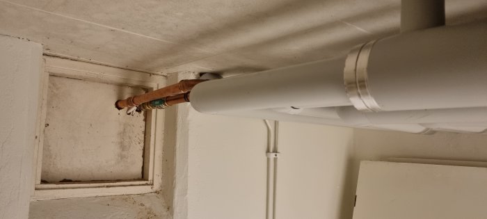 Vit ventilationsslang fastsatt i taket med kopplingsrör och ventil vid en väggkant.
