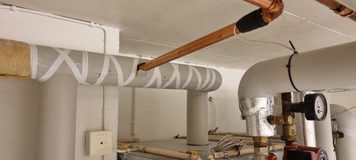 Isolerade rör och en värmeväxlare med mätare i en värmesysteminstallation.