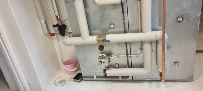 Värmesystem med vita PVC-rör, en blå Vatette-kran, Altech pump, och temperaturmätare på en betongvägg.