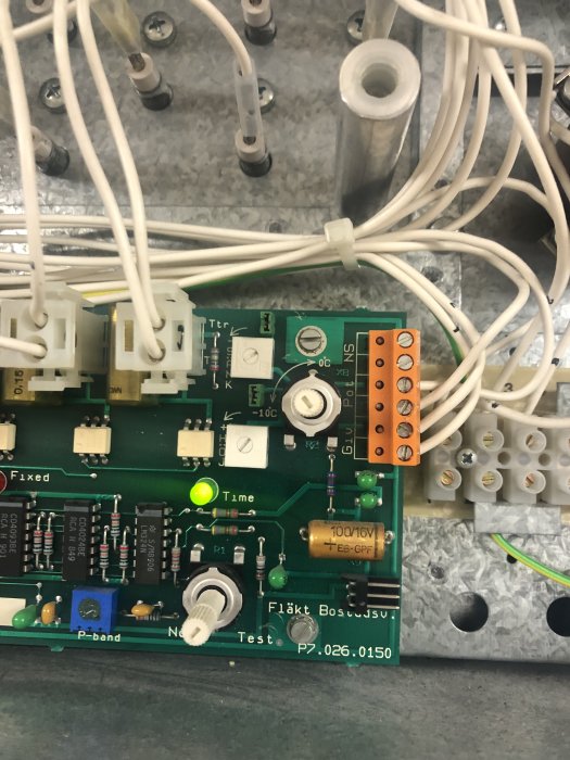 Kretskort med skruvkontakter märkta "NS" vid orange kontaktdel, omgivet av vit kablage och elektroniska komponenter.