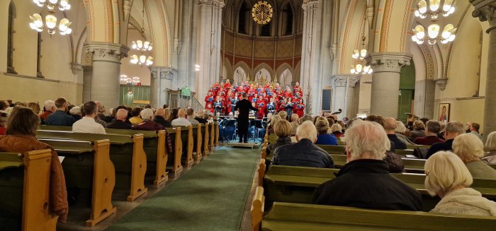 Kör framför publik i kyrka under julkonsert med dirigent och musiker.