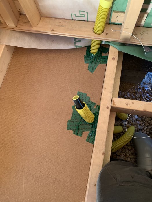 Genomföring av gula flexrör i träbjälklag och tejpade tätningselement för en renoverad golvkonstruktion.
