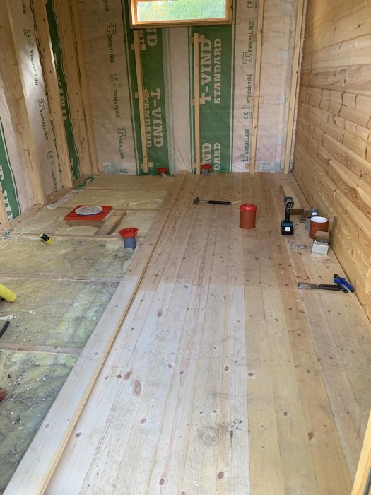 Nyinstallerat trägolv i ett rum under renovering med isolerade väggar och verktyg utspridda på golvet.