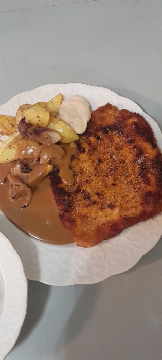 En tallrik med schnitzel, klyftpotatis, svampsås och bearnaisesås.