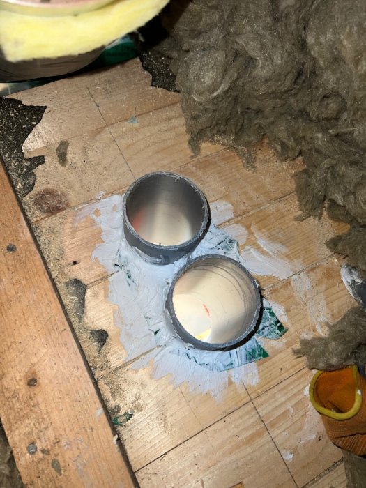Genomföringar i ett golv med två tätt åtslutna rör täckta med fog, omgivna av isolering och träytor under renovering.
