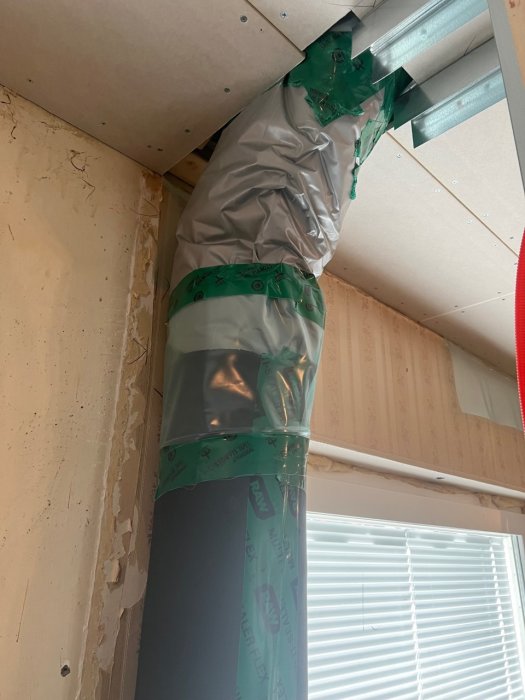 Isolerade ventilationsrör med tejpade genomföringar i taket intill plywoodvägg under renovering.