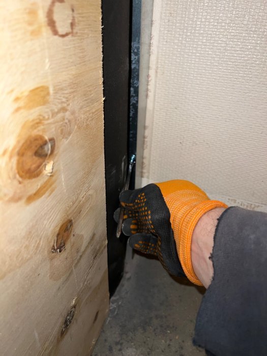 Hand i bygghandske som arbetar med montering av isolering i en schaktvägg under renovering.