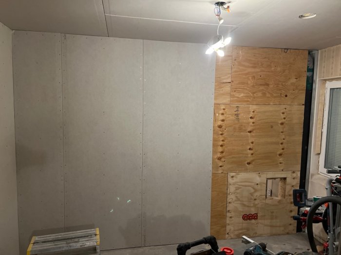 Delvis isolerad vägg med plywood och gips samt avloppsrör och förberedelse för inspektionslucka.