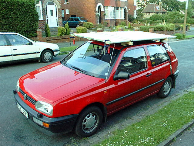 Röd bil med takräcke lastat med byggmaterial parkerad vid en bostadsgata.