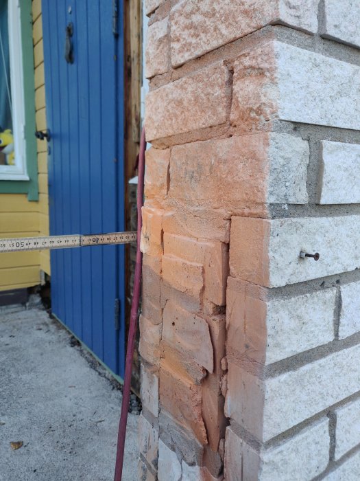 Skadat hörn på tegelvägg med måttband som visar skadans omfattning.