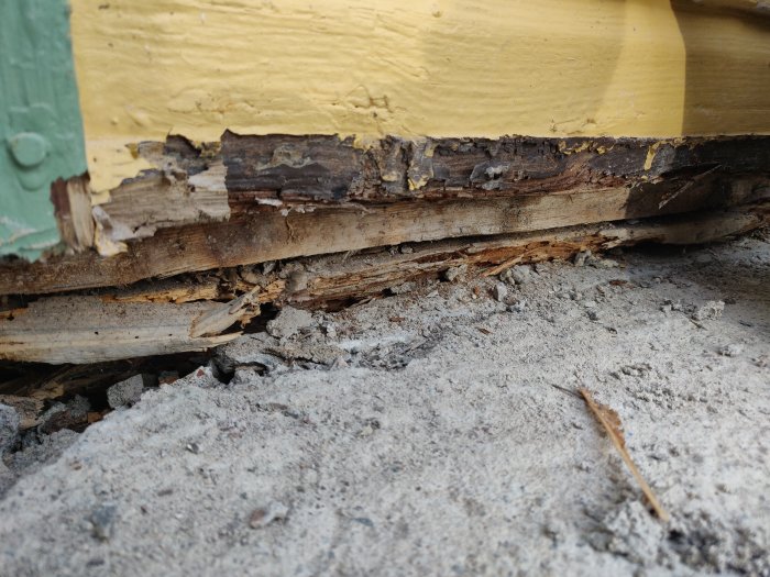 Skadad träfot på hus med flagnande gul färg och tecken på röta.