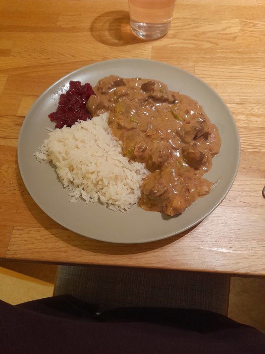 Kycklinglevergryta med champinjoner, purjolök, bacon och kapris serverad med ris och lingonsylt på en tallrik.