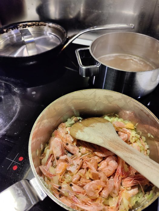 Tillagning av fiskgryta med räkor i kastrull på spis, fond reduceras i bakre kastrull.