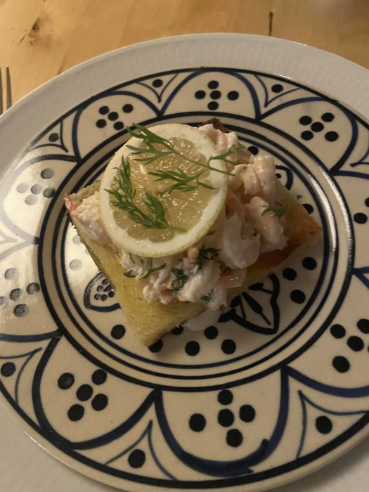 Skagenröra på en rostad brödskiva med citronskiva och dill på mönstrad tallrik.