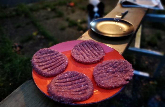 Fyra hamburgare av högrevsfärs på en orange tallrik i utomhusmiljö.