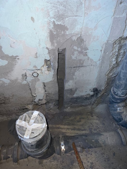 Grov spårning i betonggolv för golvvärmeslang med synliga rör och fördelarskåp i ett under renovering badrum.