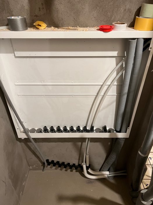 Installation av golvvärmefördelarskåp med utgående rör och sladdar i väggkonstruktion.
