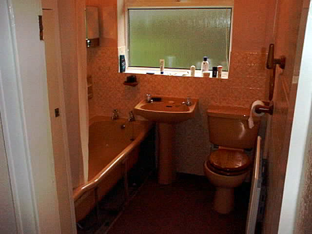 Ett gammalt engelskt badrum med champagne-rosa badkar, handfat, toalett och heltäckningsmatta.