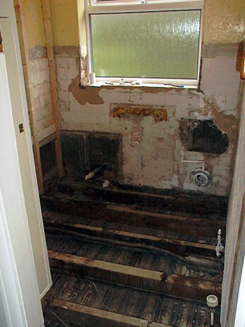 Renoverat badrum under arbete, golvbjälkar synliga, väggar delvis kala och fukt- och mögelskador.