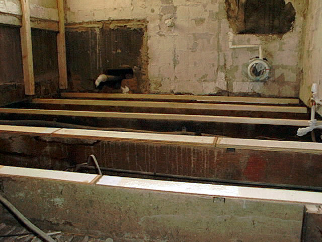 Renoveringsarbete med nya reglar installerade på ett upprivet golv, bredvid en gammal varmvattencistern.