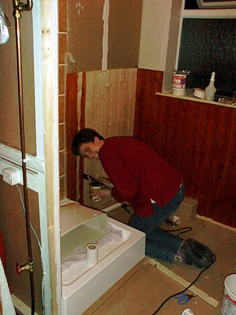 Person som installerar tvättställ i badrum med träpanel och vit duschkabin.