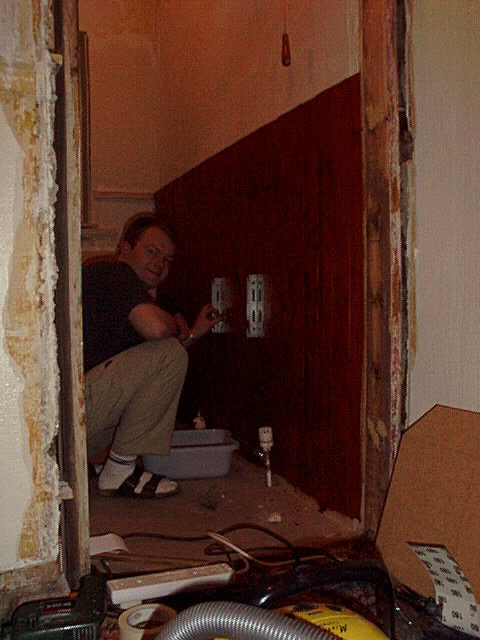 Person som arbetar på en renovering i ett rum med röda väggar, installerar eluttag vid en vit bottenplatta.