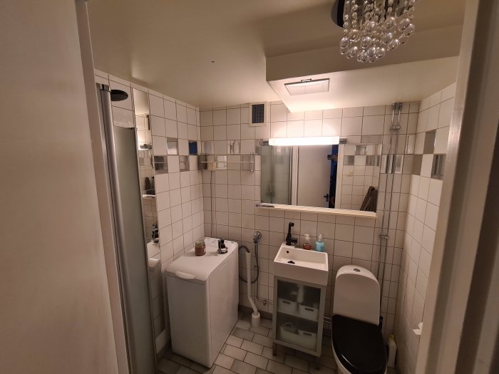 Vit kaklad badrum interiör med dusch, handfat, spegel och toalett.