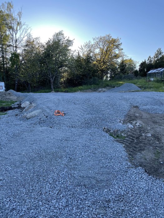 Grusgrund med synligt berg i hörn av framtidigt byggprojekt, omgiven av grönska.