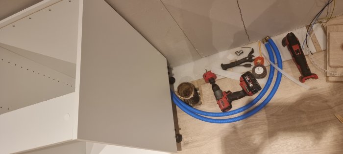 Hörn av ett rum under renovering med synliga verktyg, blå kabelskyddsrör och byggmaterial på golvet.