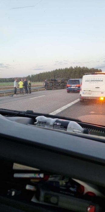 Trafikolycka med vält fordon på vägen, människor och fordon står vid sidan.