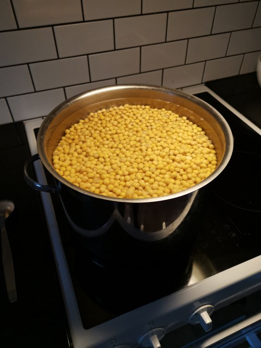 En kastrull med gula ärter på spis, vit kakelvägg i bakgrunden. Matlagning, förberedelse för ärtsoppa, köksmiljö.