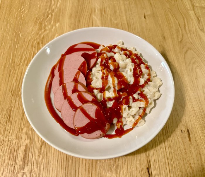 En tallrik med skivad falukorv och makaroner täckt av ketchup, en klassisk svensk rätt.