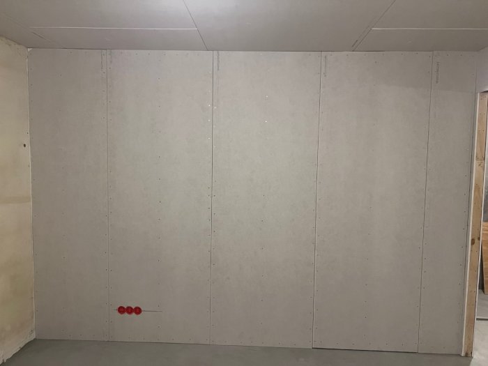 Vägg med gipsskivor i ett oavslutat rum, synliga skruvar, byggarbetsplats, isolering delvis synlig.