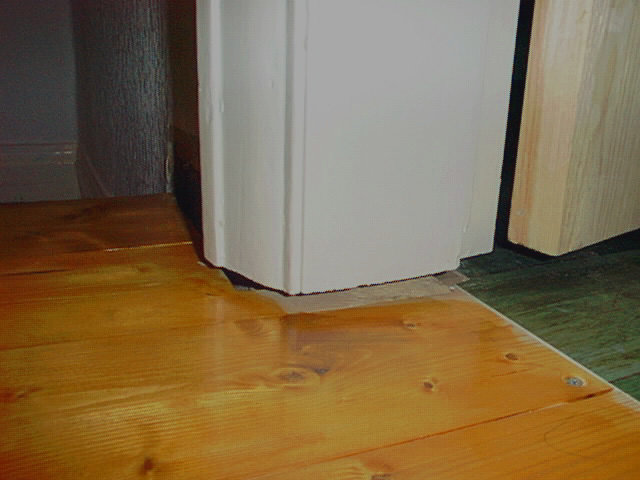 Trägolv och vit kylskåp med en synlig vattenskada vid basen.