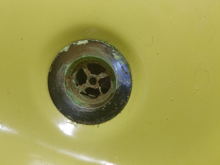 Närbild av sliten gul handfat med metallsil och rostiga fläckar.