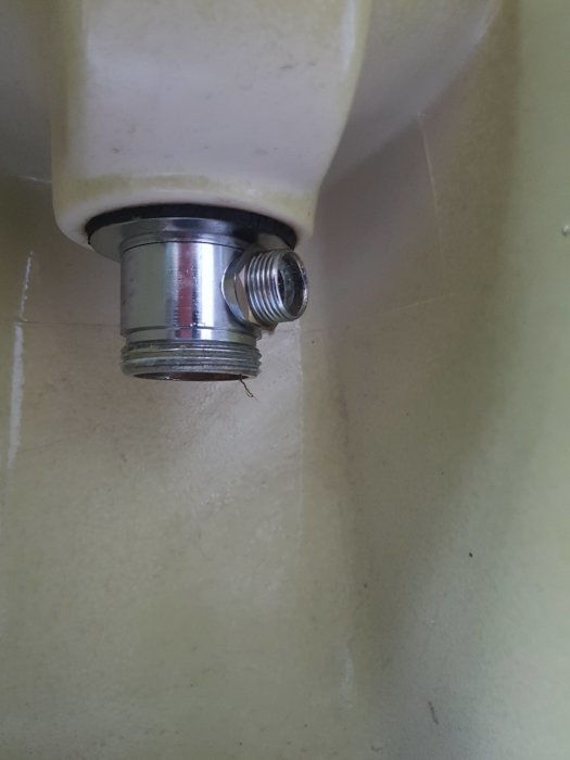 Metallanslutning av vattenrör till vitmålad apparat, möjlig fuktskada syns, behöver rengöras.