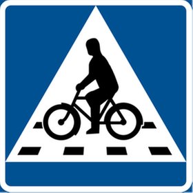Triangulär skylt, blå bakgrund, vit kant, symbol för cykelöverfart med cyklist och övergångsställe.
