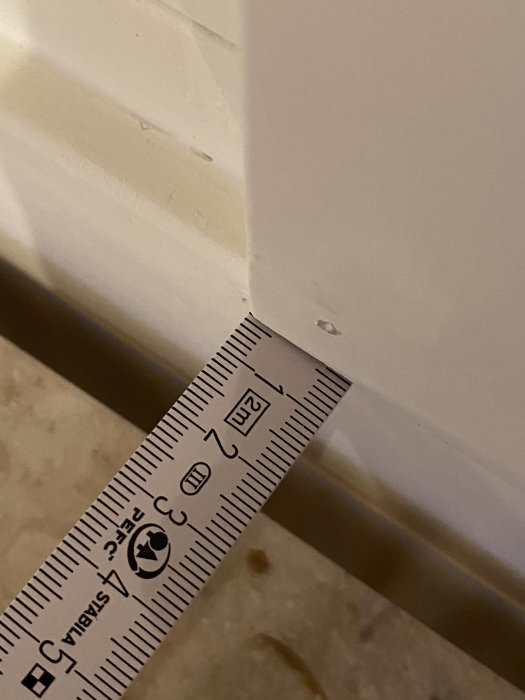 Ett måttband mot ett dörrfoder och golv för mätning av avståndet eller glipan.