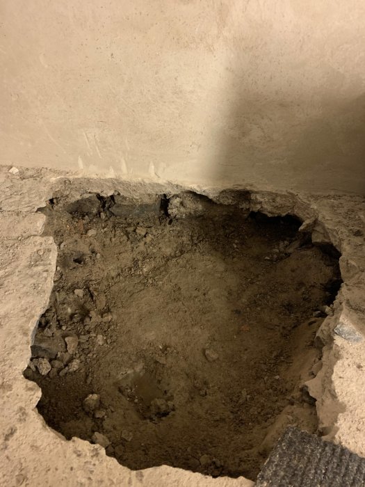 Ett hål i en betonggolv med synliga jord och grus, skadad yta, byggarbetsplats eller renovering.